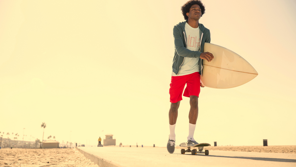 urban culture meets surf and skate world, surfer, riding a skateboard down to the beach with surfboard in hand